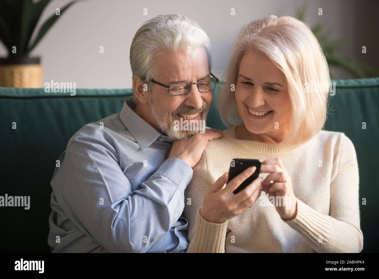 Mature attractive couple sitting on couch using smartphone Stock Photo