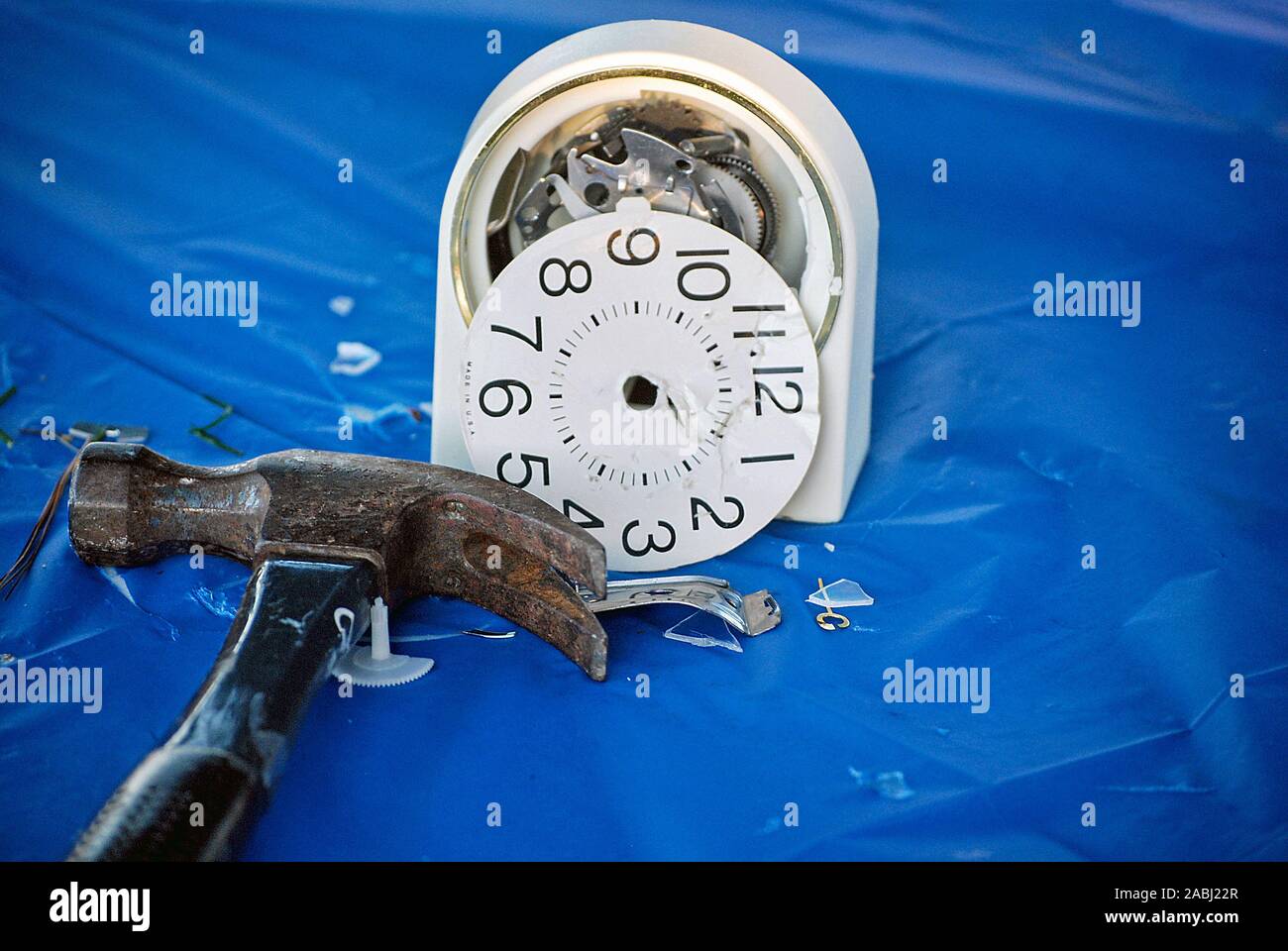 hammer with pieces of smashed alarm clock on blue plastic Stock Photo