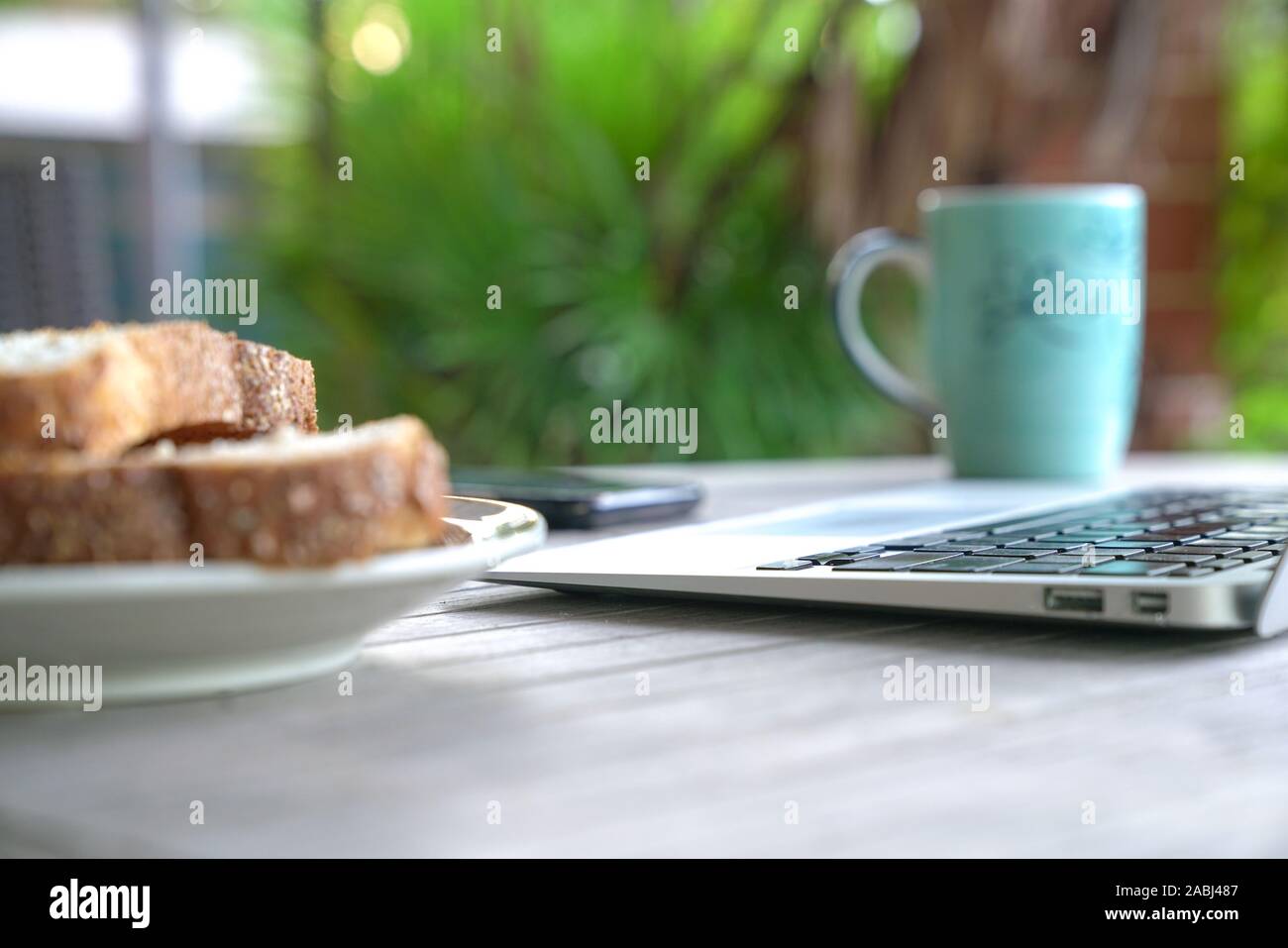 Working on the computer and cell phone while having breakfast. Work from home or flexi time concept. Stock Photo