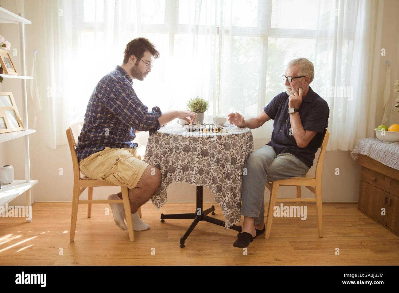 Young man and elder old man playing chess board game together at home. Stock Photo
