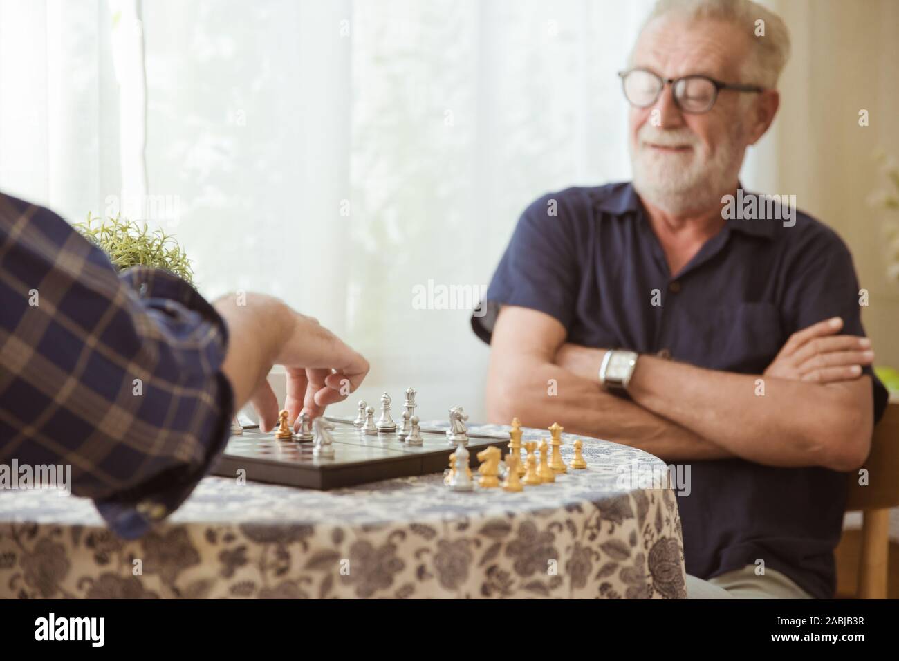 Smart Elder playing Chess board game at home for training brain memory and thinking happy smiling selective focus at chess piece. Stock Photo