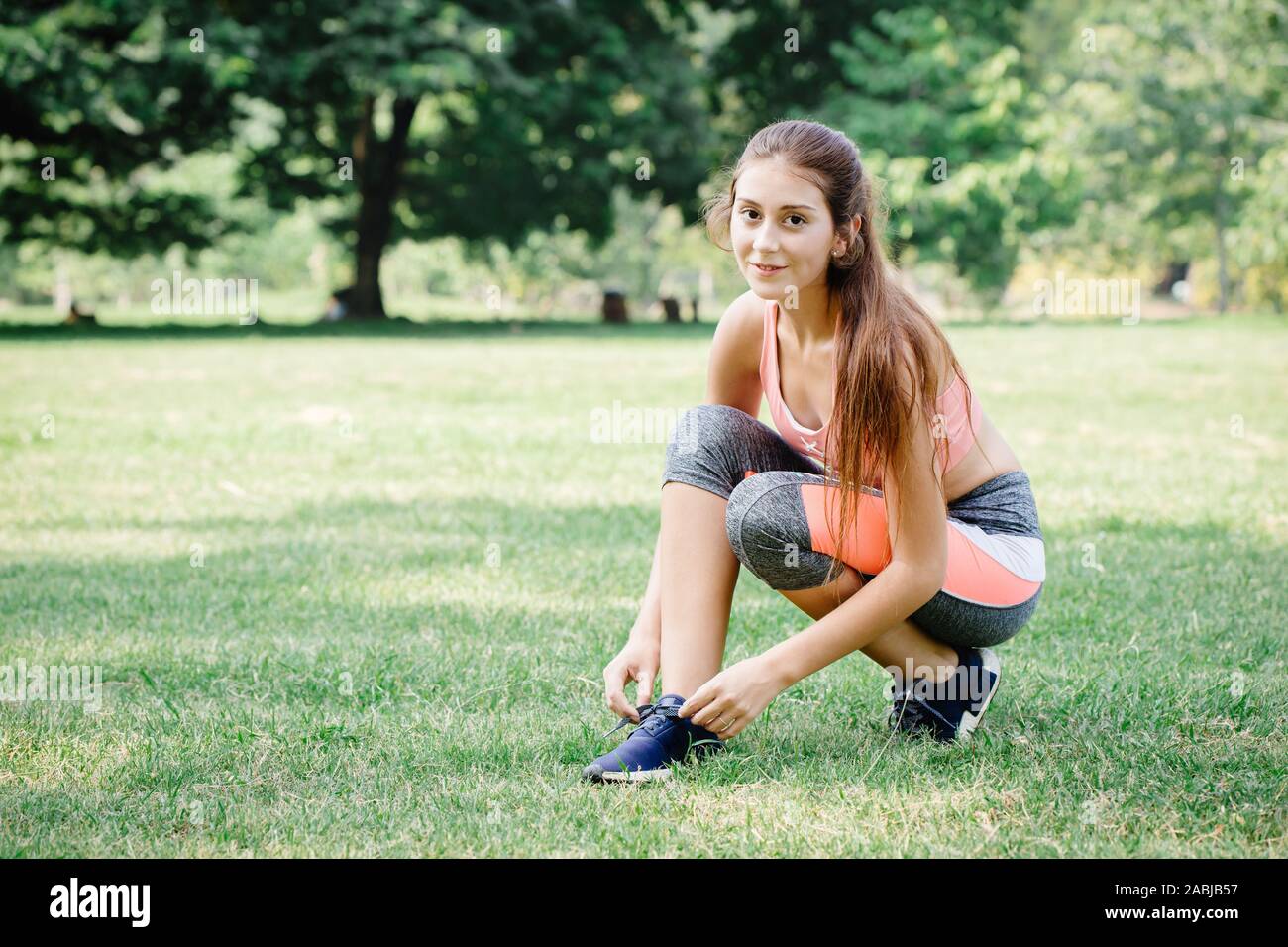 Beautiful sport exercise fit girl tie her shoe at outdoor green park. Stock Photo