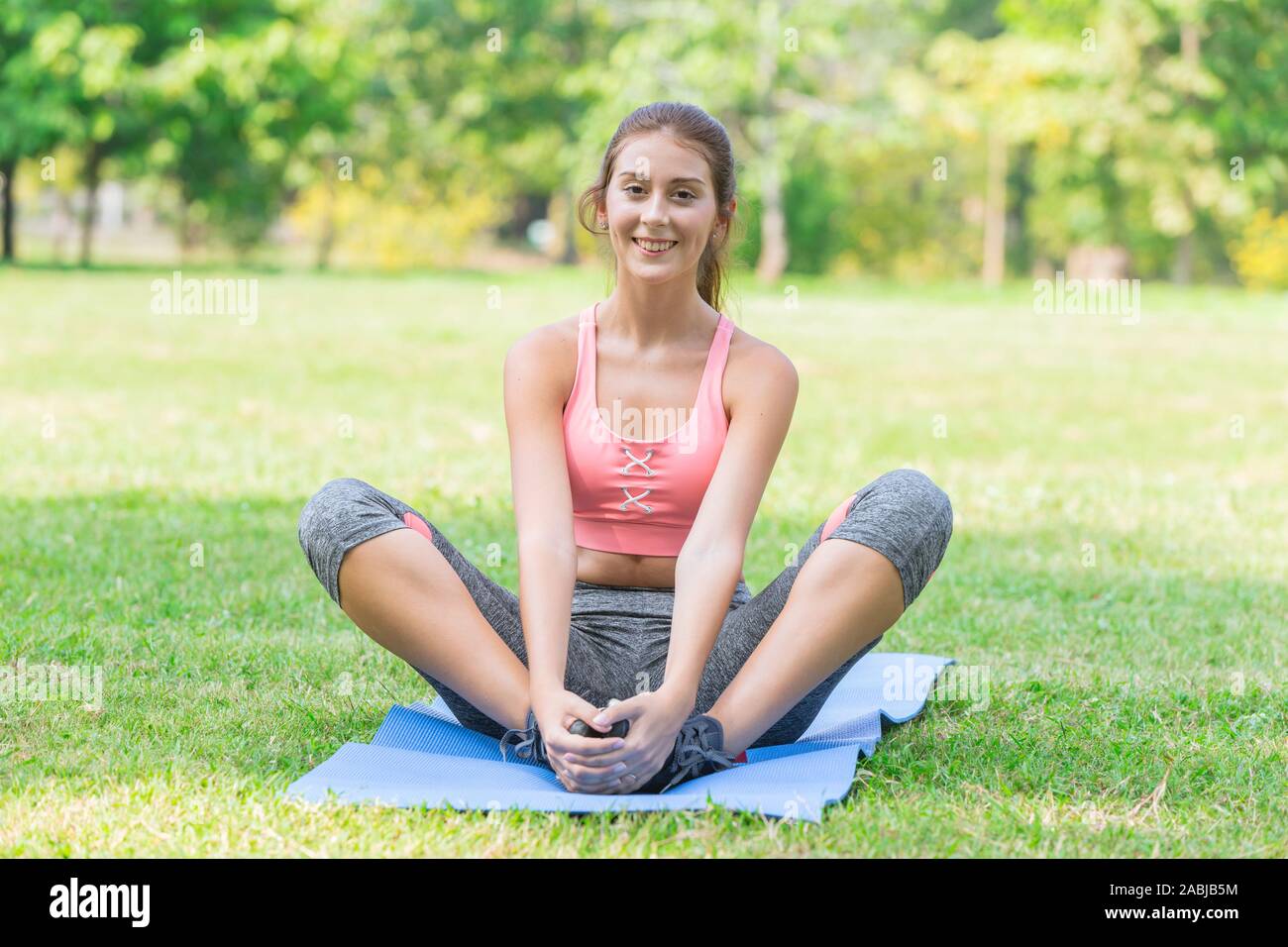 cute young healthy sport teen sitting smiling on yoga mat outdoor park garden. Stock Photo