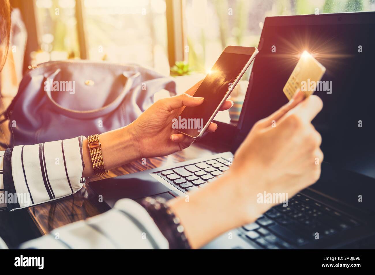 Businesswoman using mobile phone making credit card online payment on her phone app with laptop computer background. Stock Photo