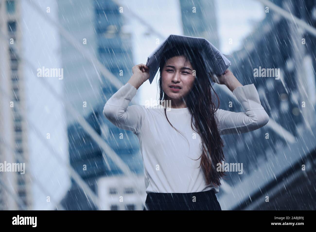 Girl in the heavy rain storm cover head with newspaper for economic obstacle passing concept. Stock Photo