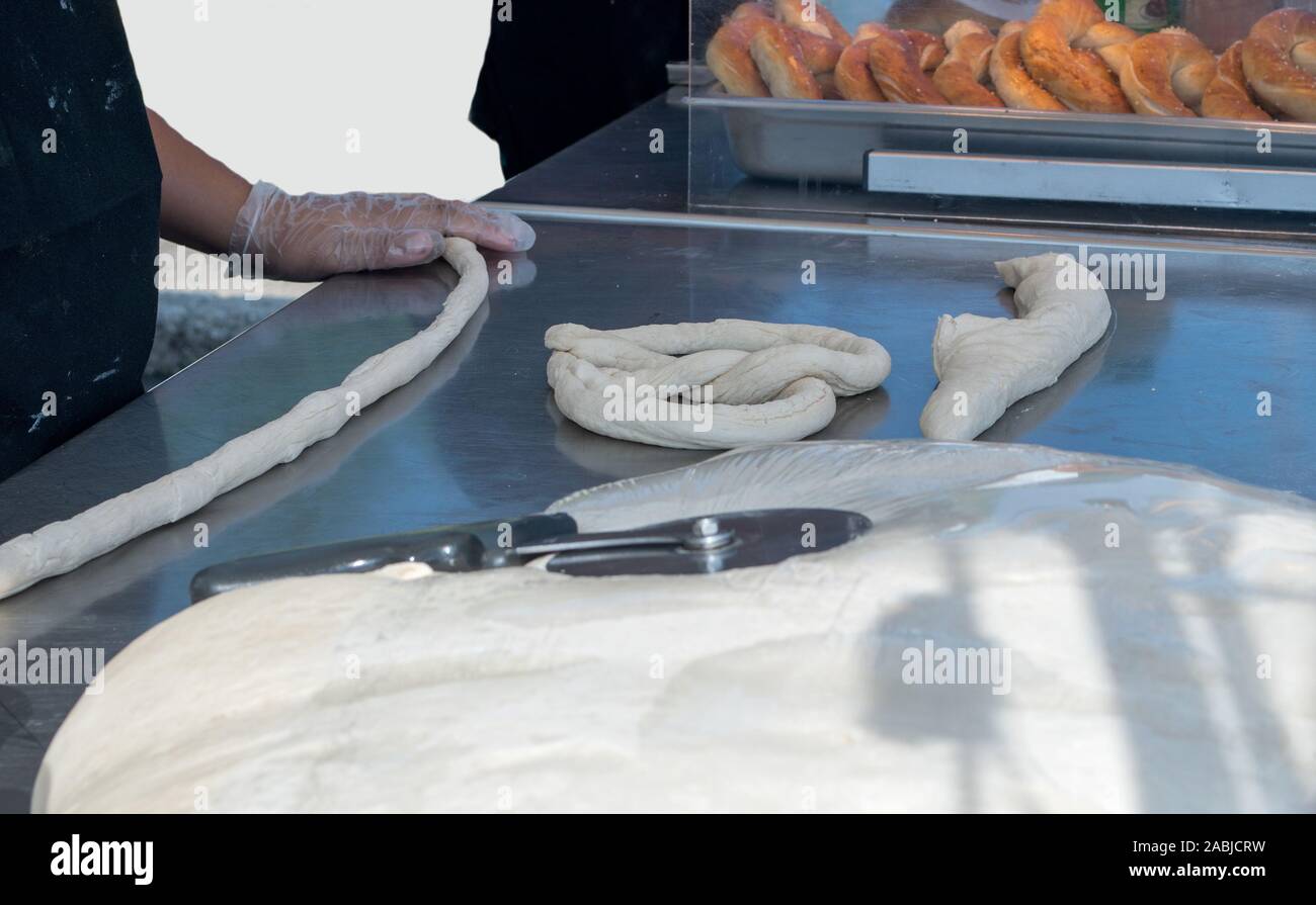 A baker rolls raw dough into a rope to make a hot, soft pretzel fresh from the oven Stock Photo
