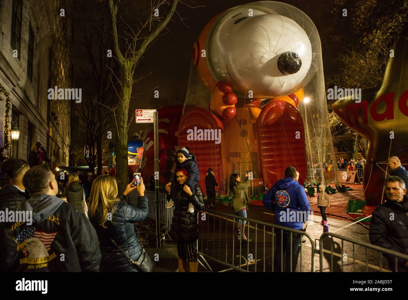 New York, NY, USA. 27th Nov, 2019. Thousands of spectators packed the streets around the American Museum of Natural History to see the inflation area for the balloons for Macy's Thanksgiving Day Parade. A family pauses for photos, with Astronaut Snoopy in the background., Credit: Ed Lefkowicz/Alamy Live News Stock Photo