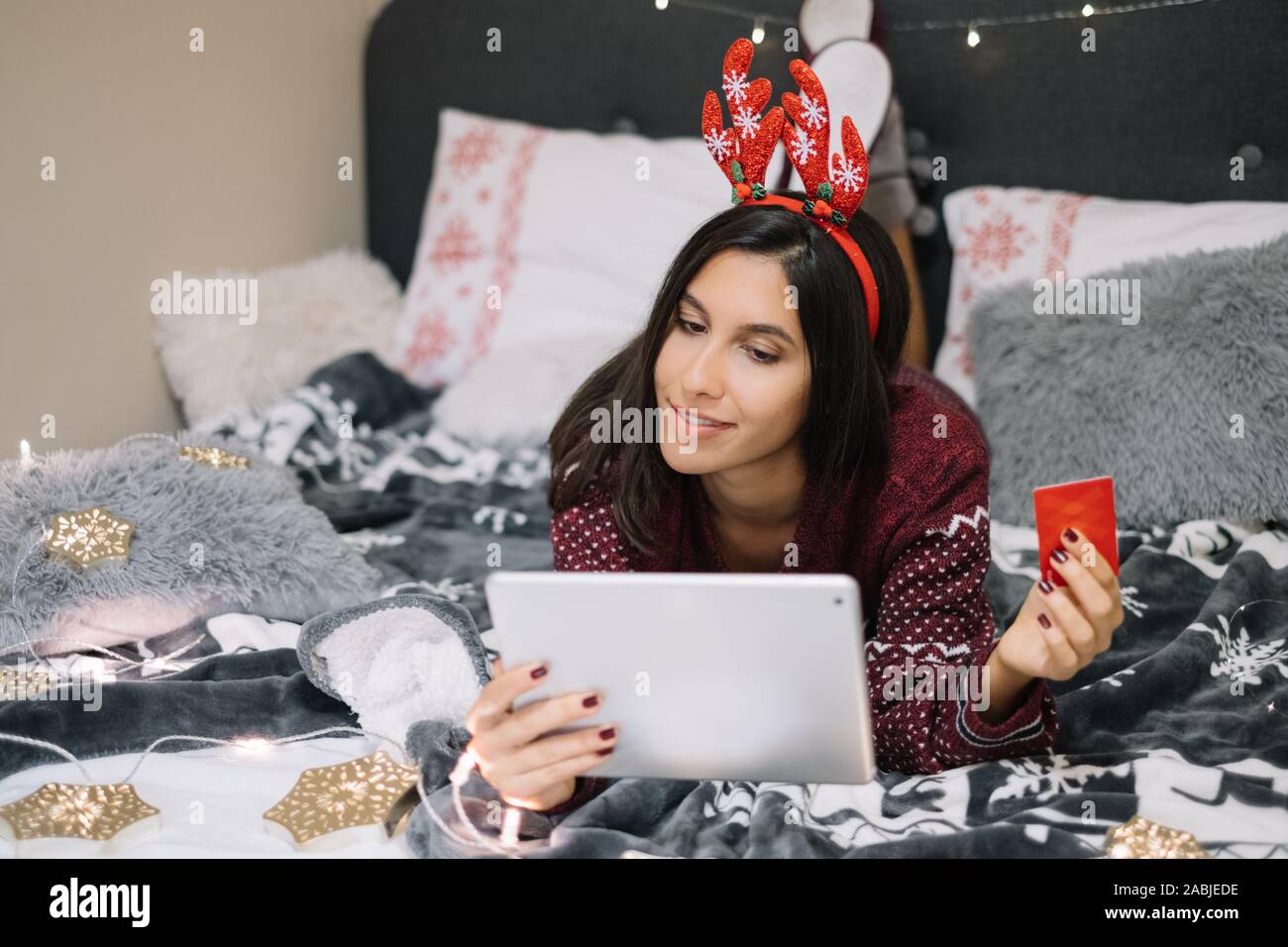 Young girl laying on stomach on bed while using tablet Stock Photo