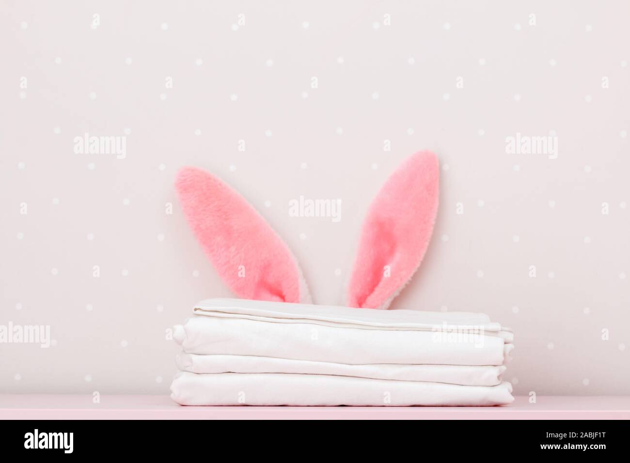 Close-up stack of clean white bedding and the Easter bunny ears, on the dressing table, on the background light walls. Copy space. Stock Photo