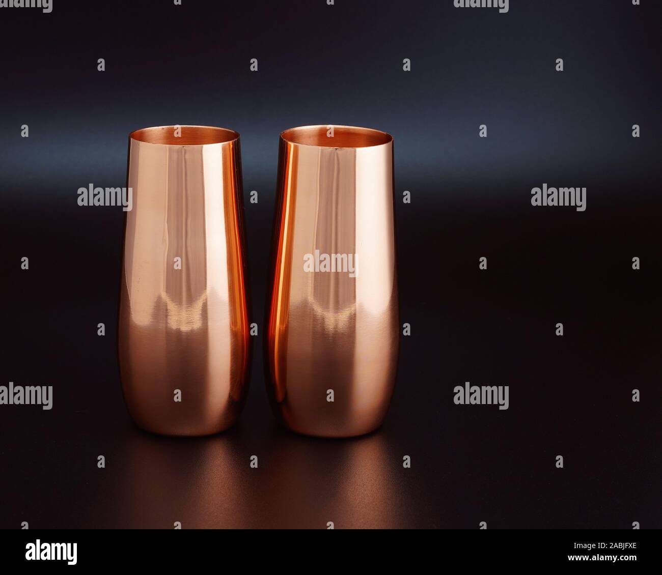 A pair of copper wine goblets burnished by soft lighting lit against a
