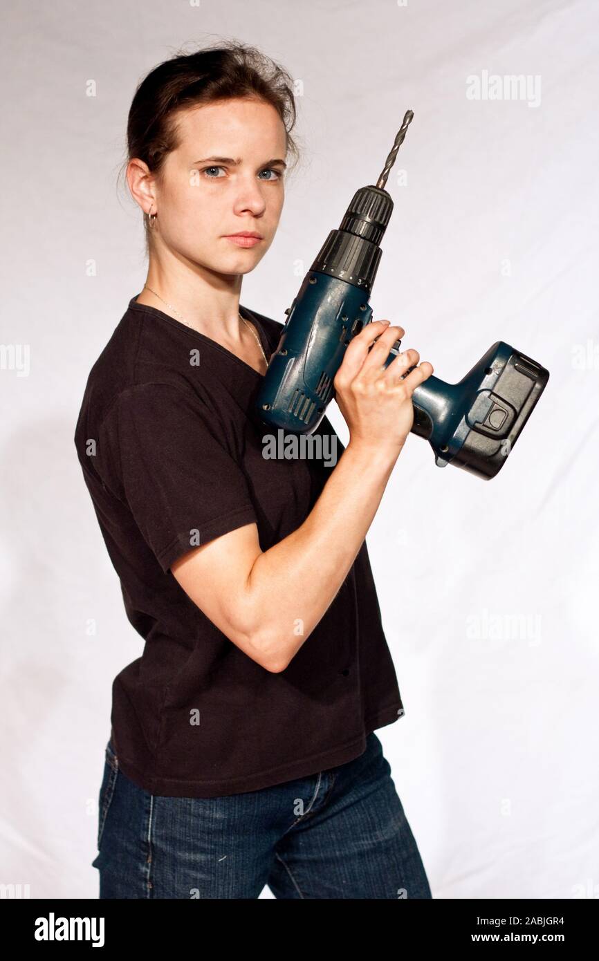 strong young woman in an black shirt holding a cordless screwdriver in front of a white studio background Stock Photo