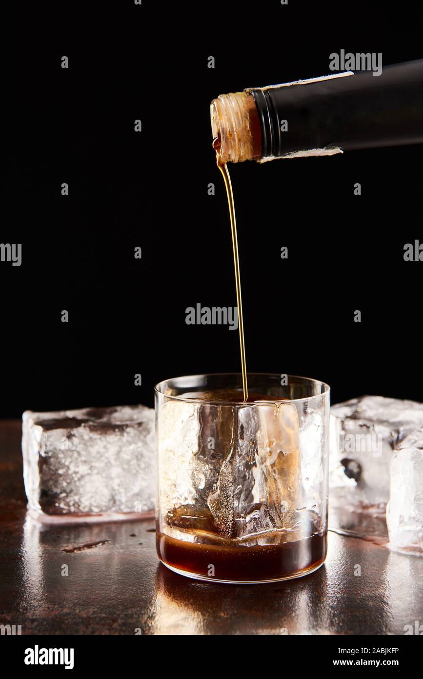 coffee liquor poring in glass with ice cubes isolated on black Stock