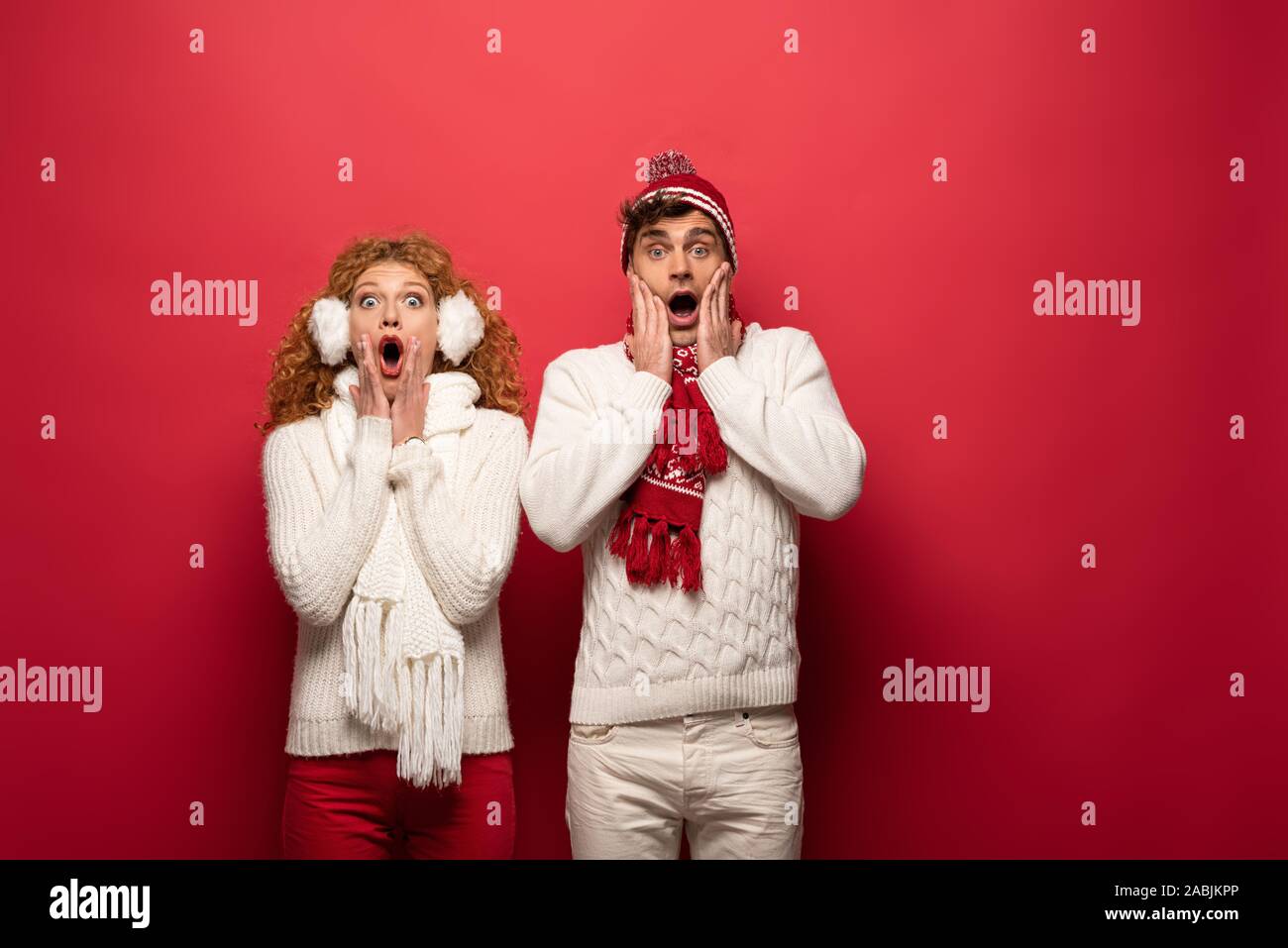 beautiful shocked couple in winter outfit isolated on red Stock Photo