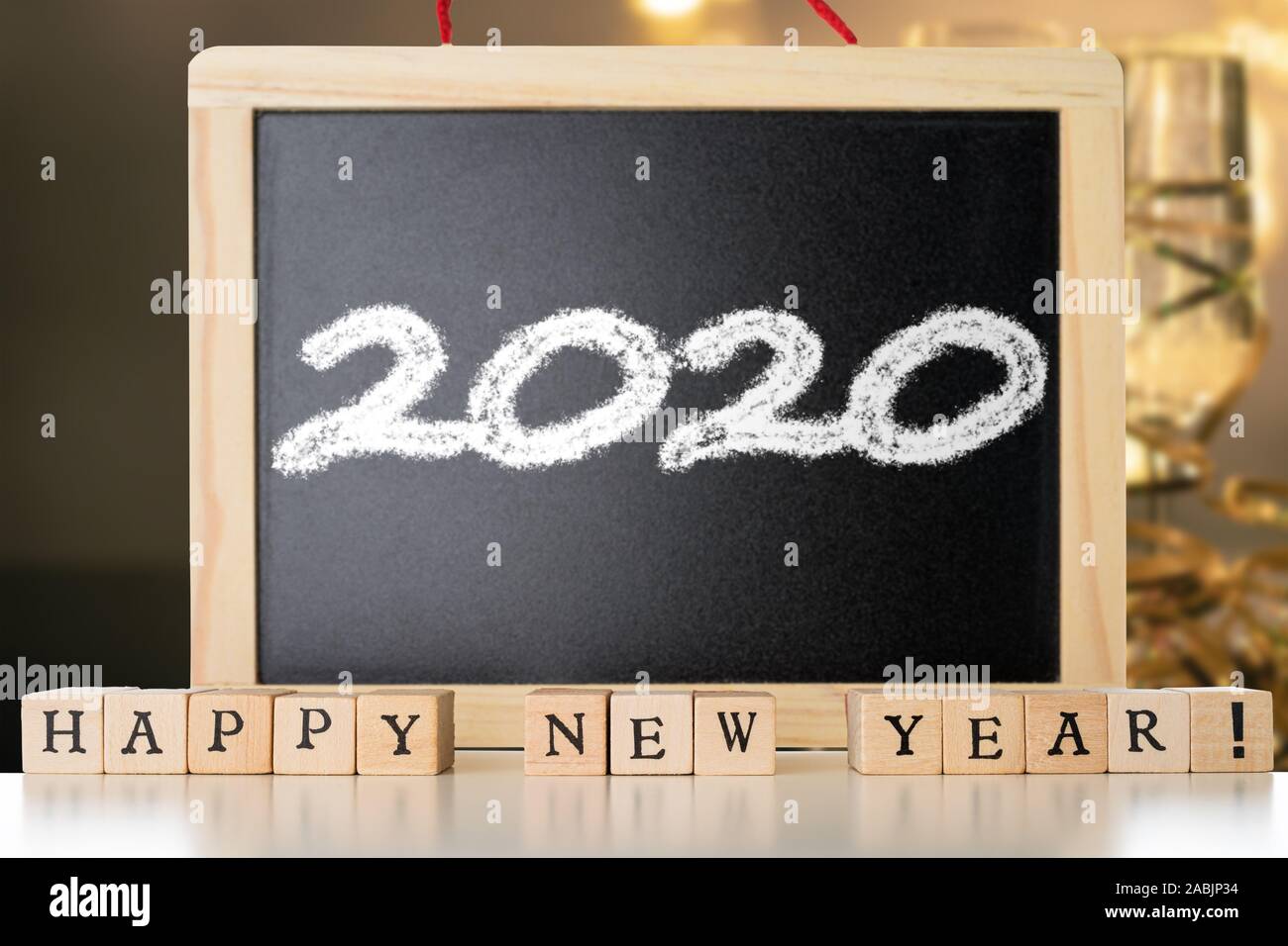 Happy New Year text made out of wooden blocks. Blackboard with 2020 text made with chalk. Two glasses of champane with festive new year's eve decorati Stock Photo