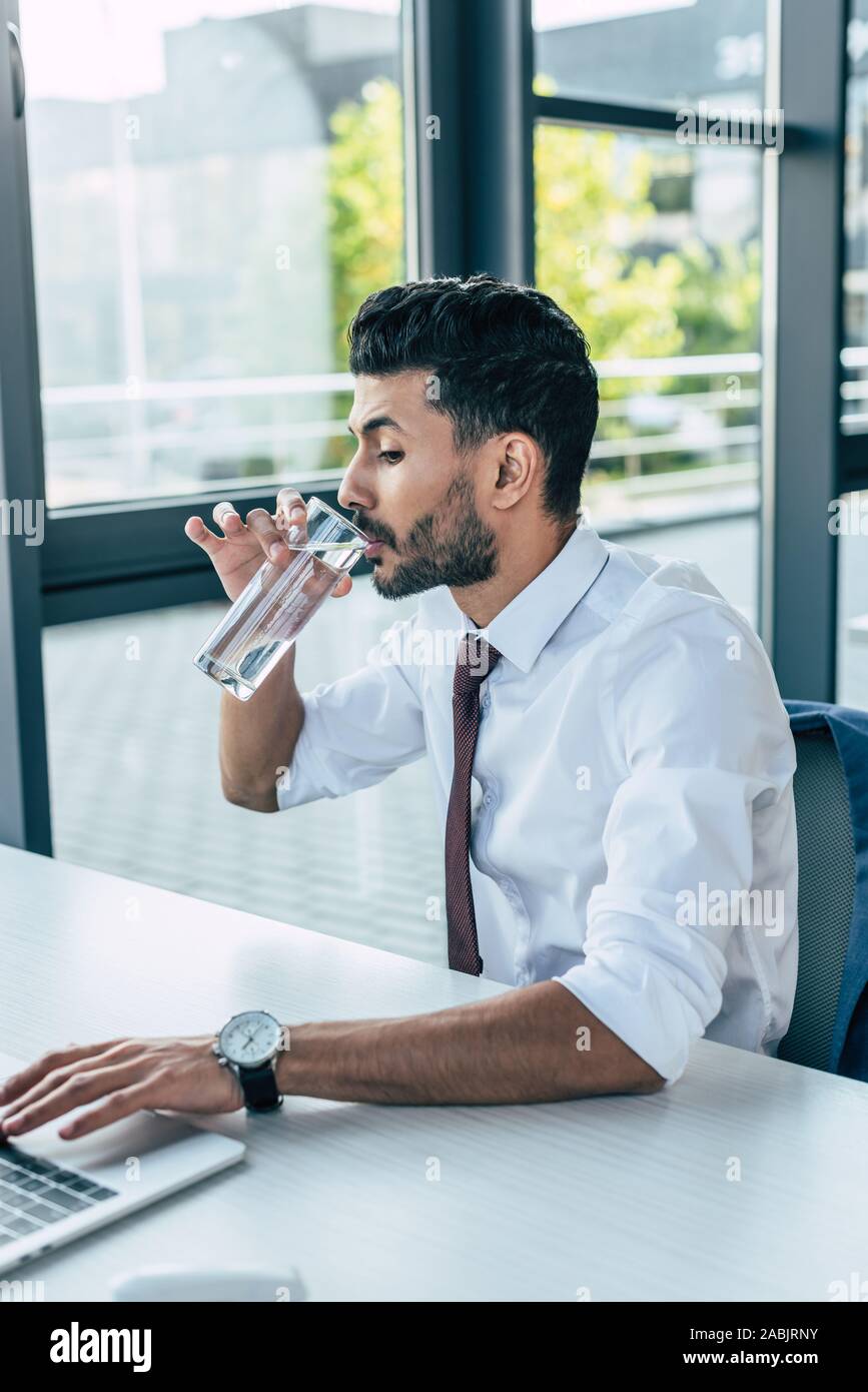 thirsty businessman drinking water while using laptop Stock Photo