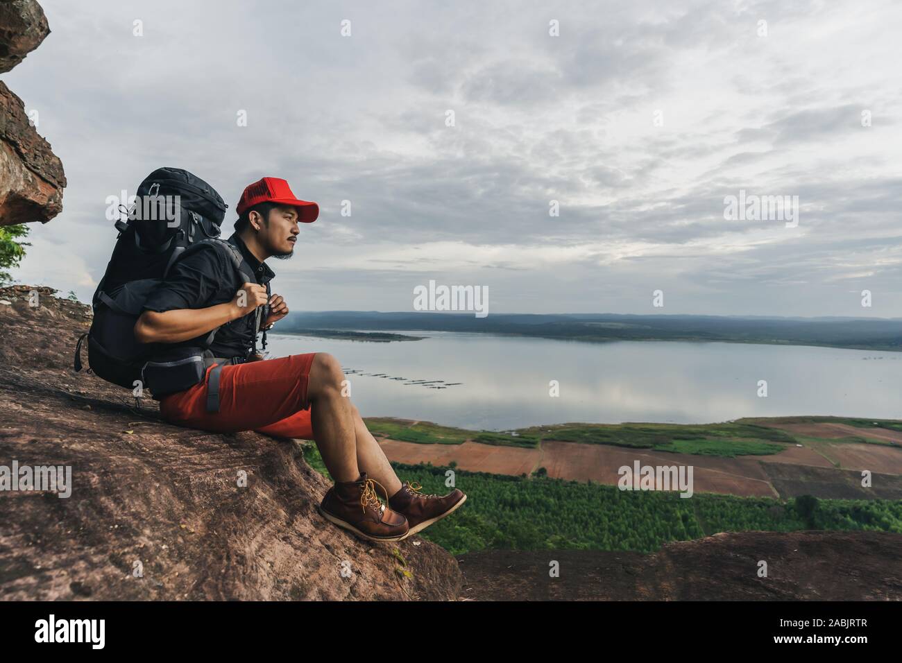 man traveler with backpack sitting on the edge of cliff, on a top