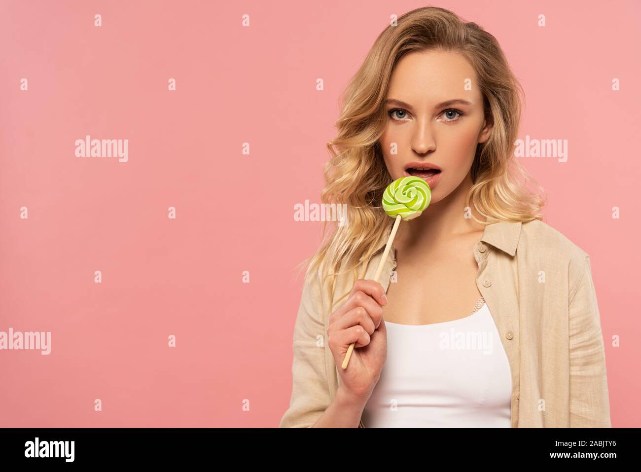 Attractive blonde woman licking lollipop isolated on pink Stock Photo