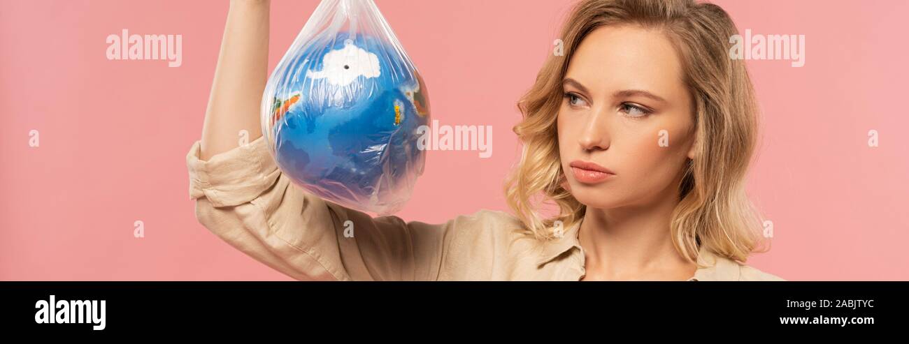 Panoramic shot of blonde woman looking at globe in polyethylene pack isolated on pink, global warming concept Stock Photo