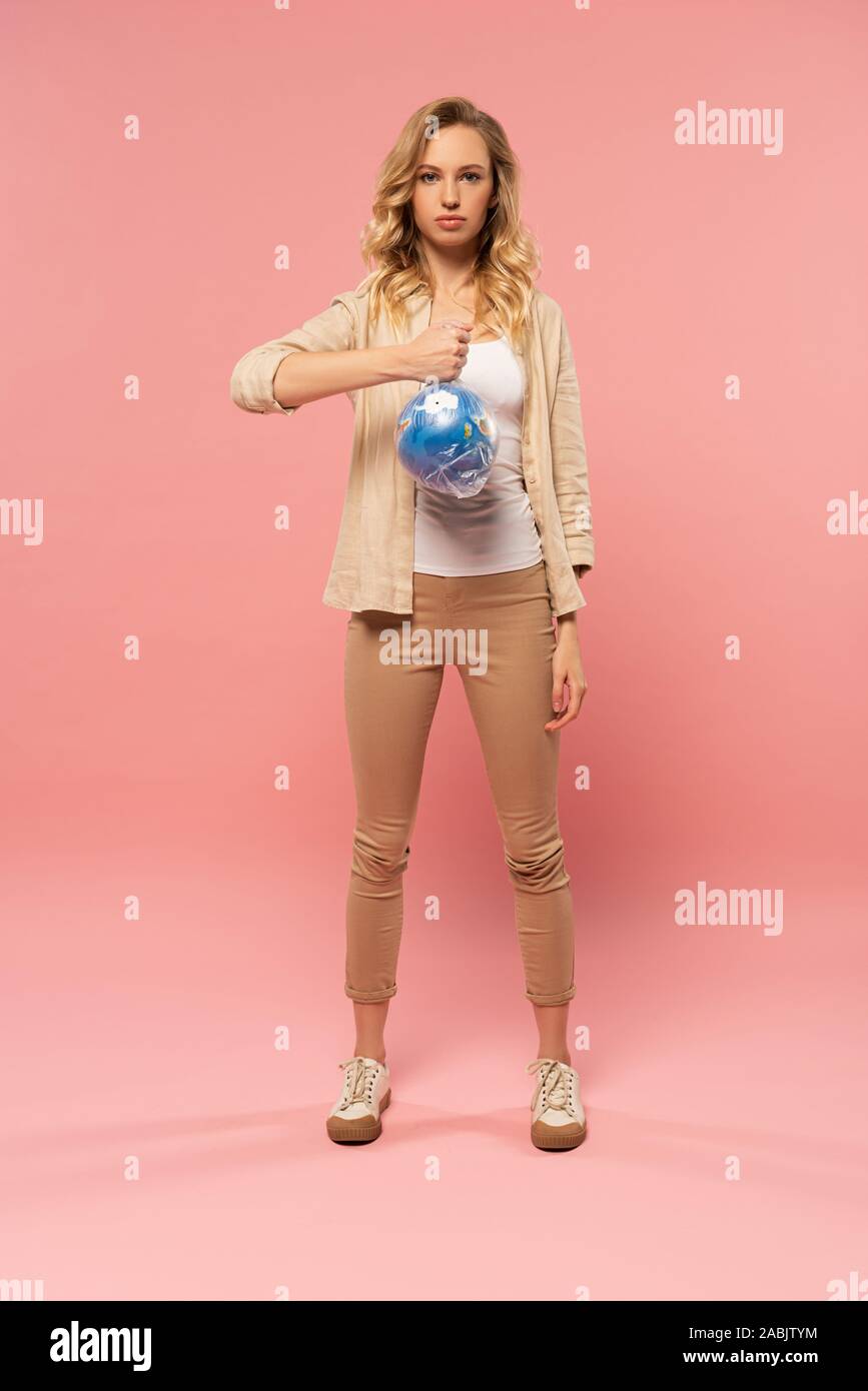 Blonde woman holding globe in polyethylene pack on pink background, global warming concept Stock Photo