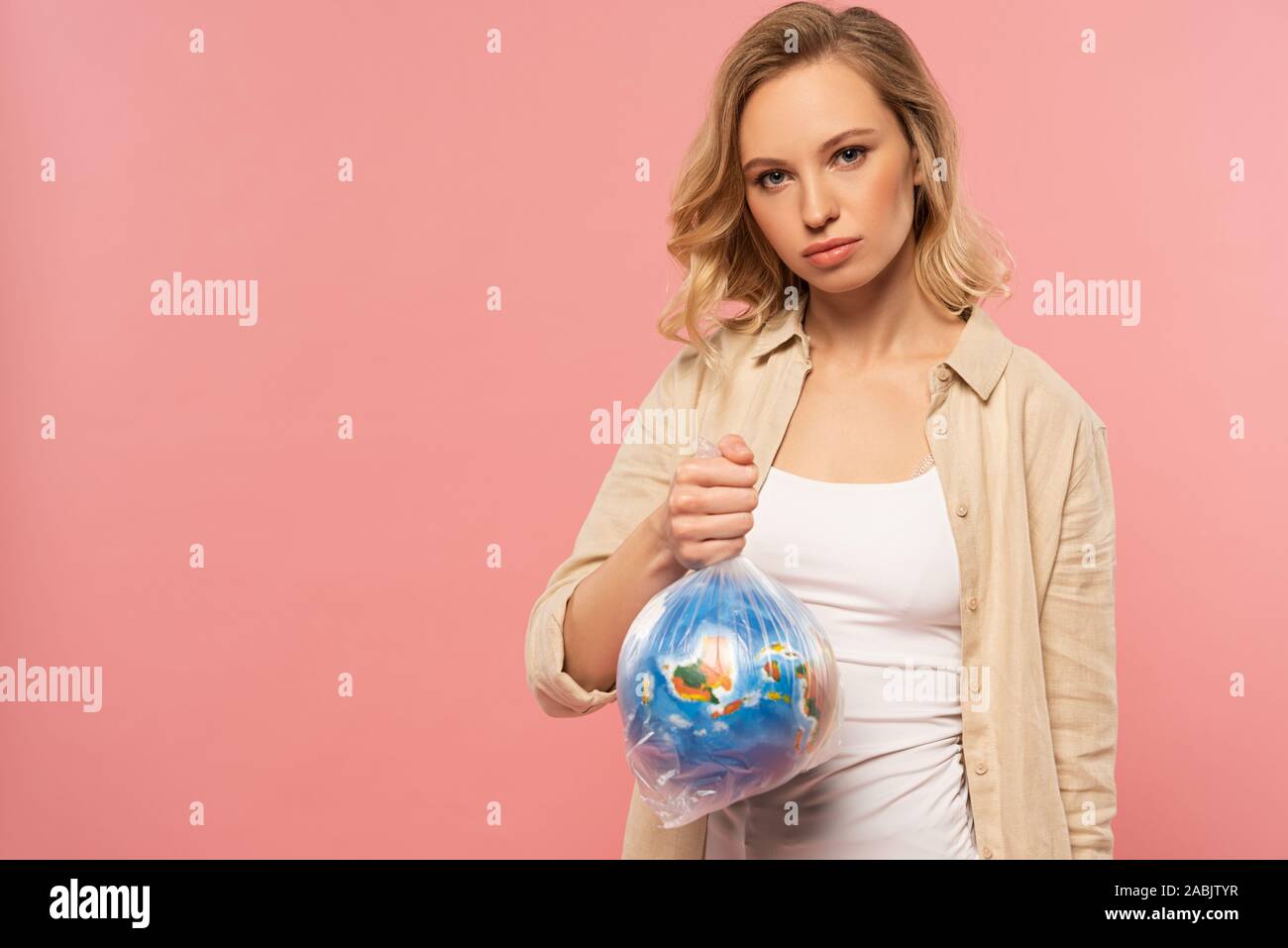 Blonde woman holding globe in polyethylene pack isolated on pink, global warming concept Stock Photo
