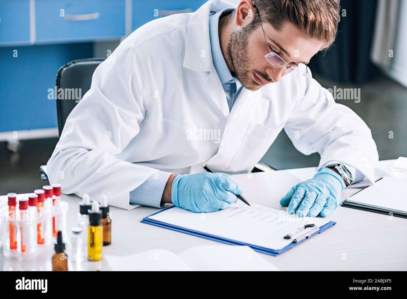 selective focus of bearded immunologist in glasses holding pen near clipboard Stock Photo