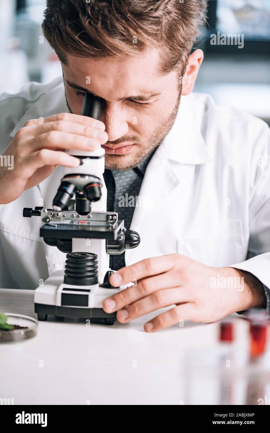 selective focus of handsome biochemist looking through microscope in laboratory Stock Photo