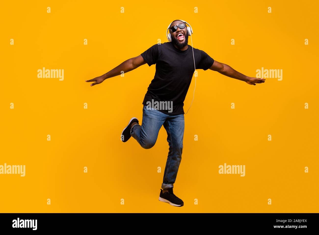 I believe can fly. Full size phtoo of funny positive afro american guy listen music with headset sing song raise hands like birds wings wear t-shirt Stock Photo