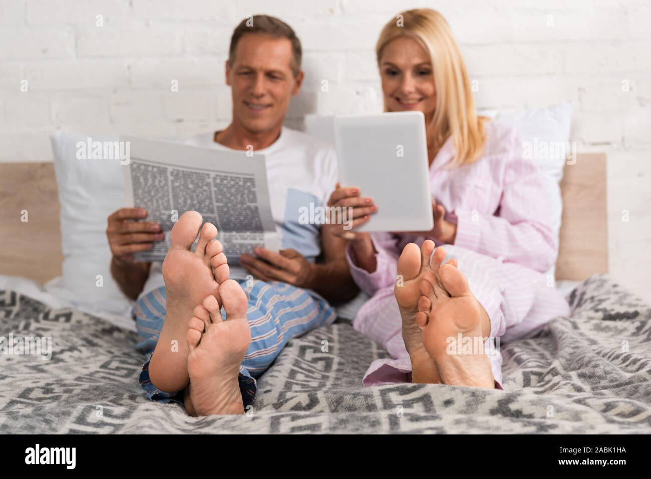 Man reading newspaper while wife using digital tablet on bed Stock Photo