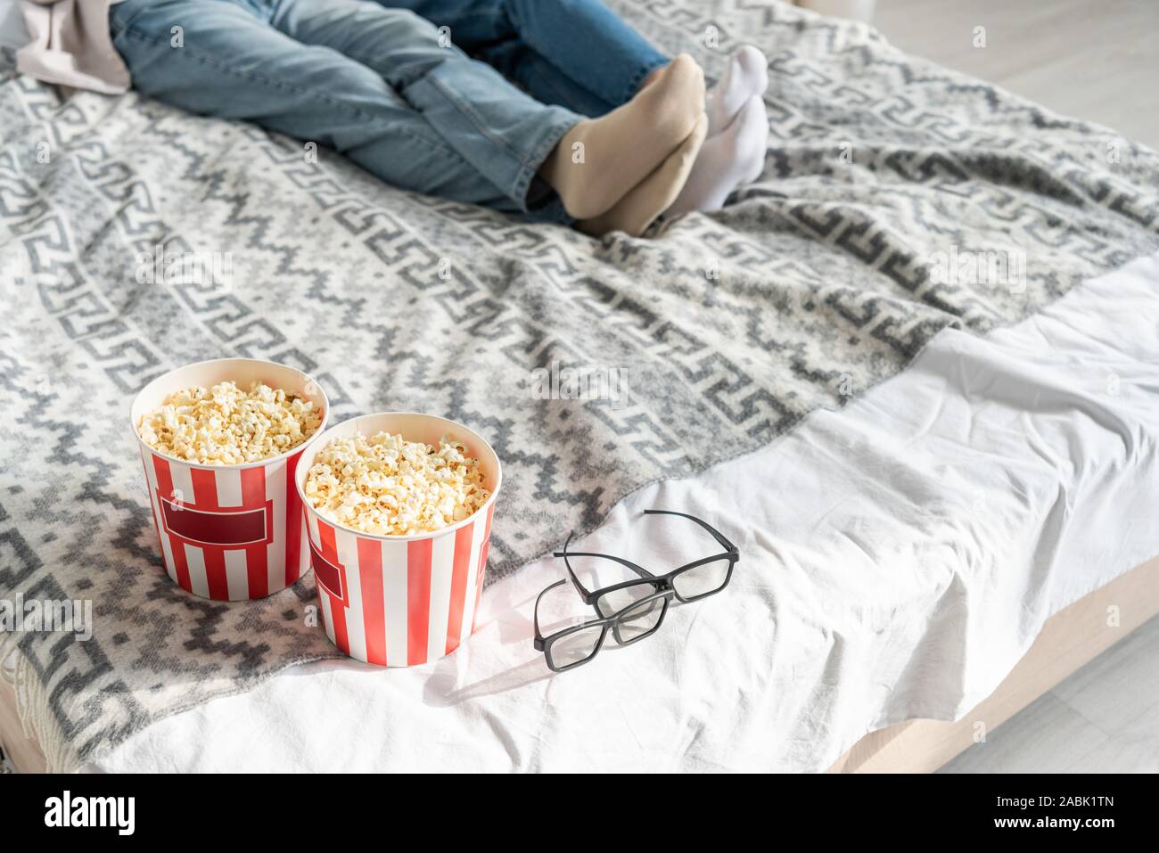 Cropped view of couple lying on bed beside popcorn buckets and 3d glasses Stock Photo