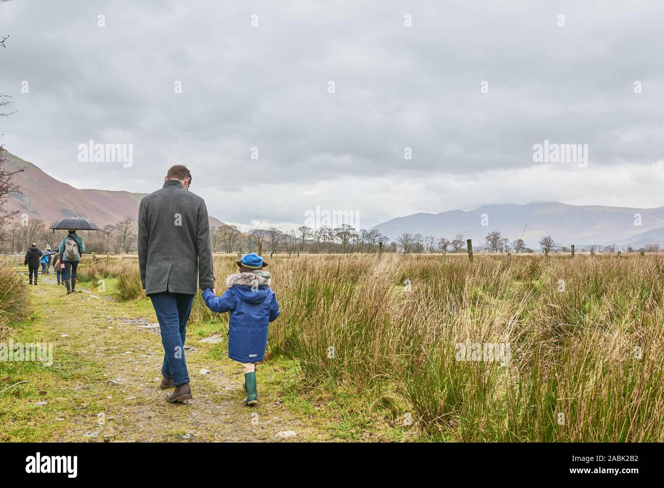 Teenage boy and young child walk hand in hand behind other members of their family along the shore of Lake Derwentwater, Borrowdale valley, Lake distr Stock Photo