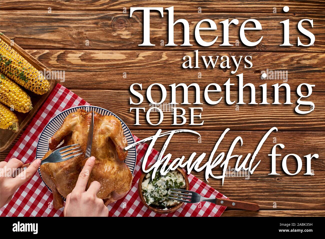 cropped view of woman cutting roasted turkey on red plaid napkin near grilled corn on wooden table with there is always something to be thankful for l Stock Photo