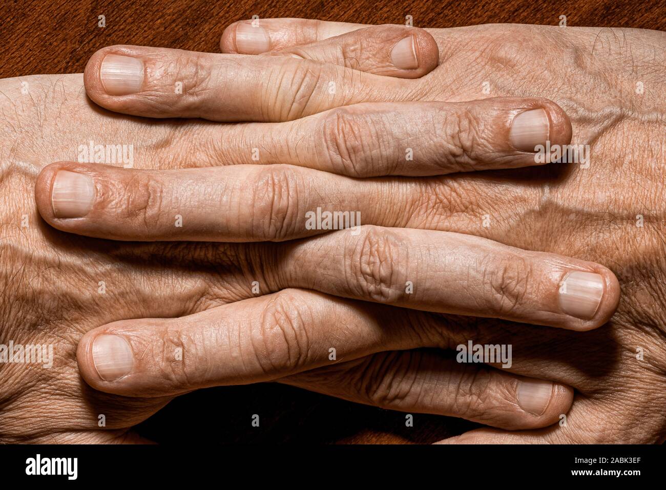 Color photo of senior man hands with crossed fingers, on a wooden background Stock Photo