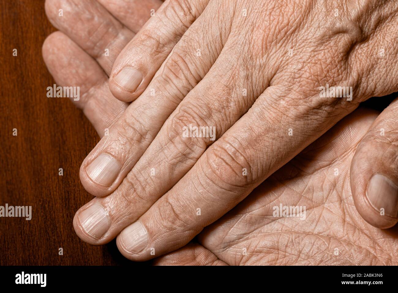 Color photo of senior man crossed hands detail on a dark wooden background Stock Photo