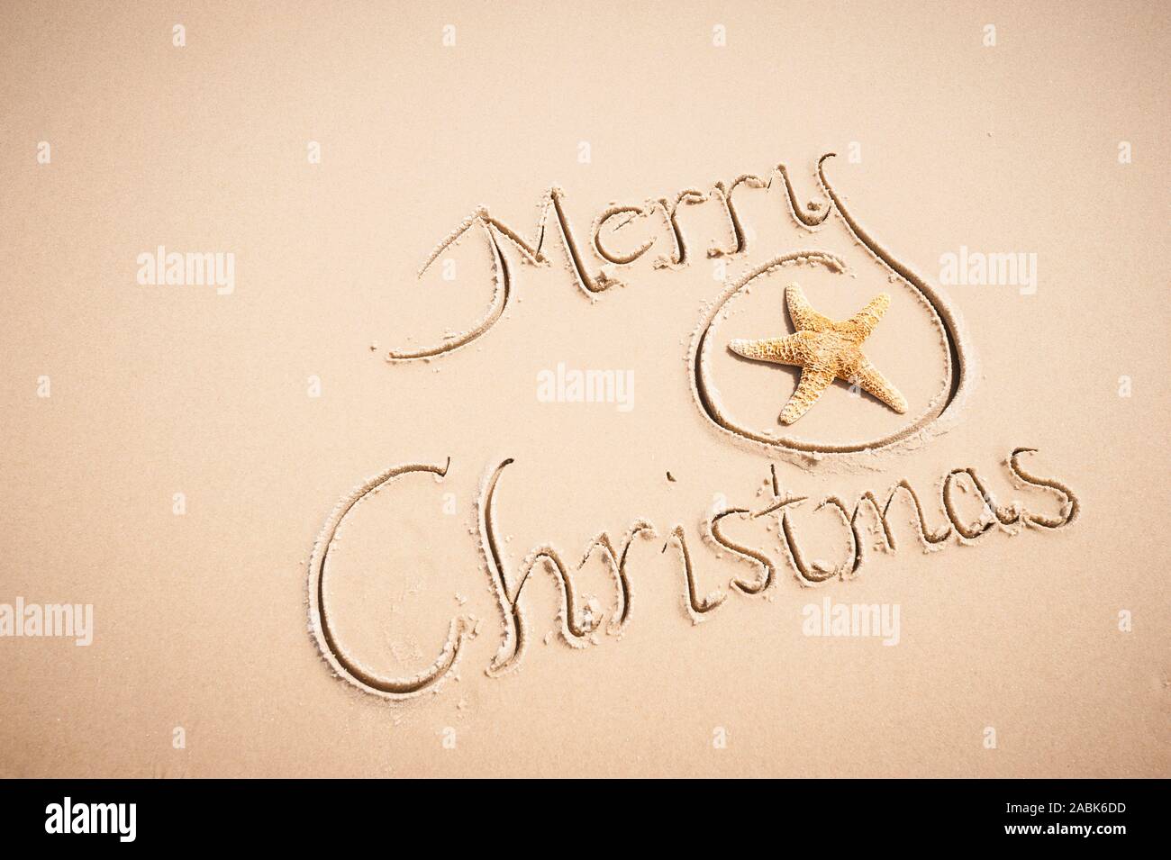 Merry Christmas message handwritten on the shore of a sunny beach with smooth sand copy space Stock Photo