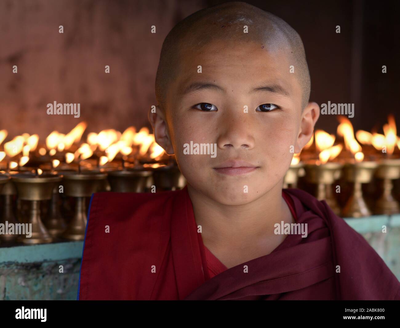 Nepali Buddhist boy monk poses for the camera in front of butter lamps at Kathmandu’s Shree Ghah Gumba Stock Photo
