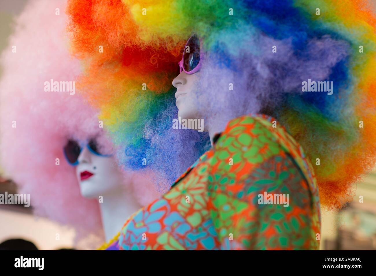 Two white mannequins wearing sunglasses with very big curly colorful wigs on their head, one pink and the other rainbow style Stock Photo
