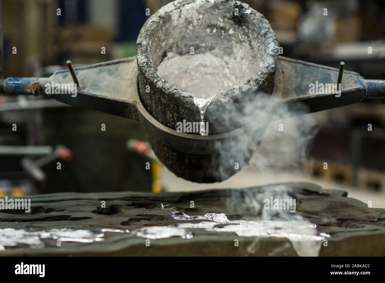 Detail of Metal casting pouring molten aluminum silver colored liquid into a mold creating smoke in a industrial envoriment, workshop space Stock Photo