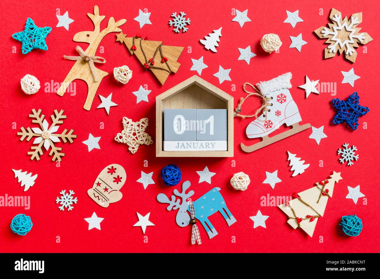 Top view of wooden calendar, holiday toys and decorations on red Christmas background. The first of January. New Year time concept. Stock Photo