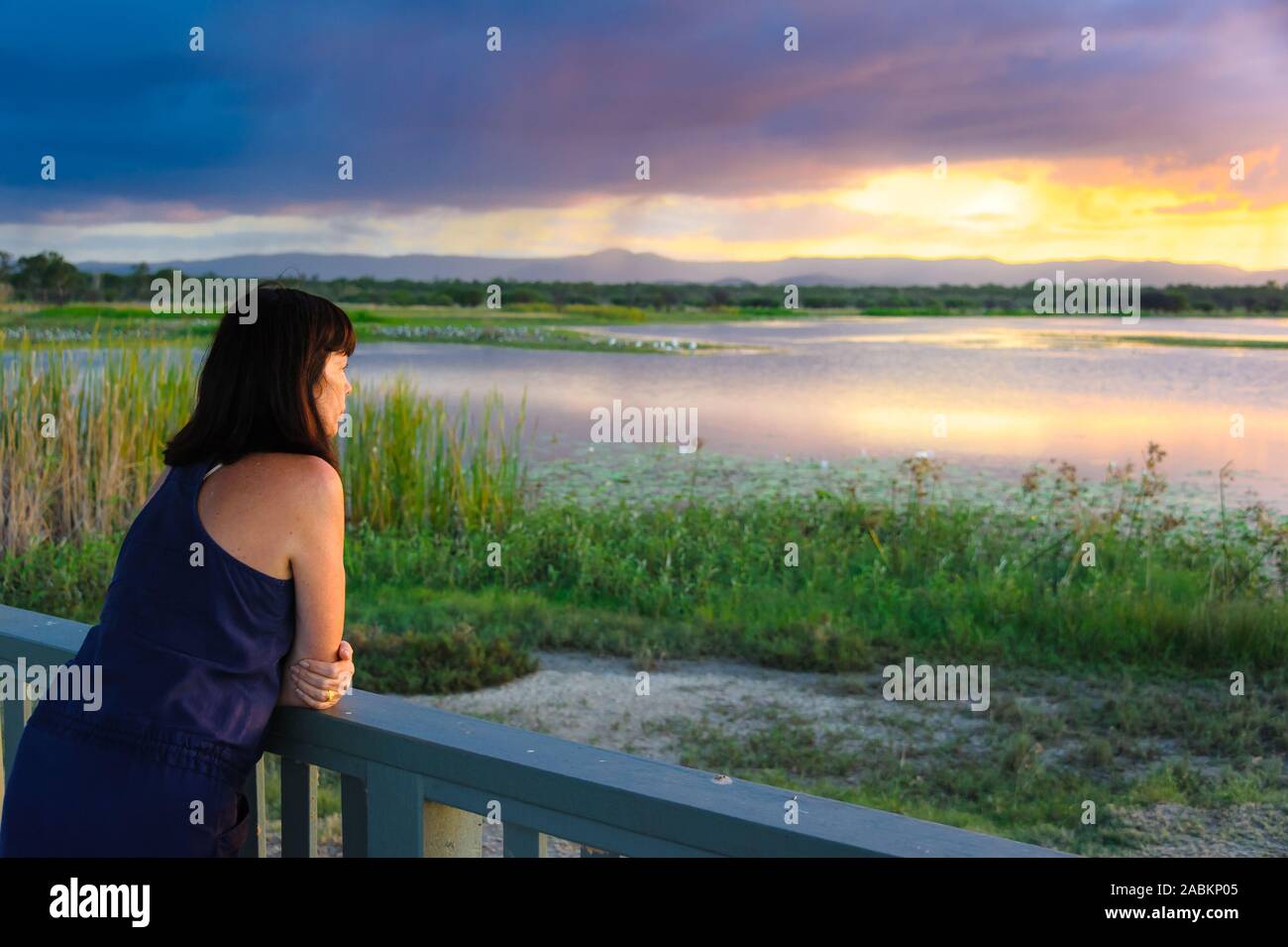 Female tourist, at sunset, leaning on viewing platform rail, at the St. Lawrence Wetlands, near Mackay, Queensland, Australia. Stock Photo