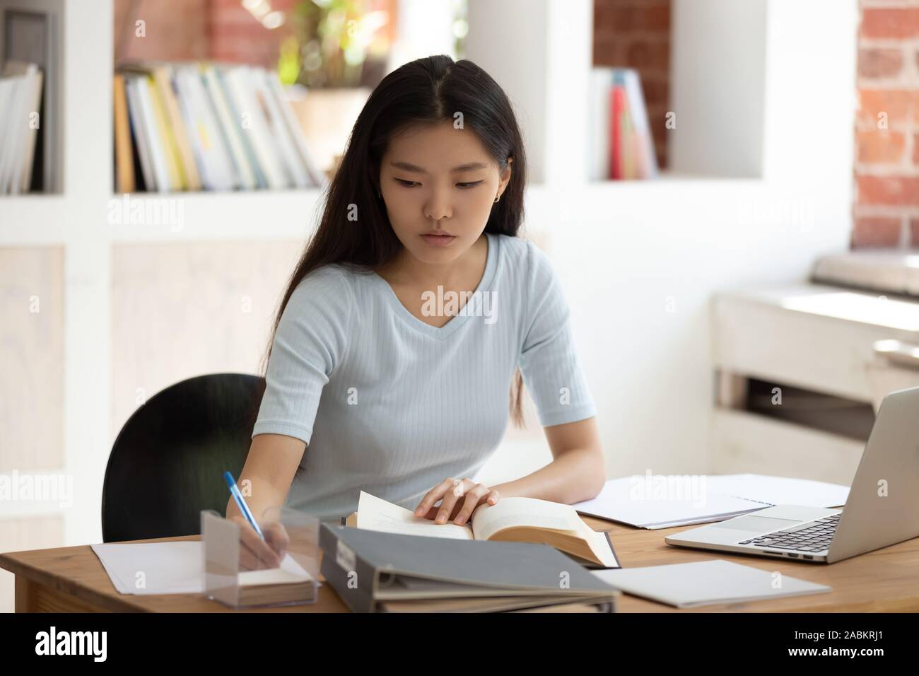 Concentrated young Asian female student sitting at desk in library. Stock Photo