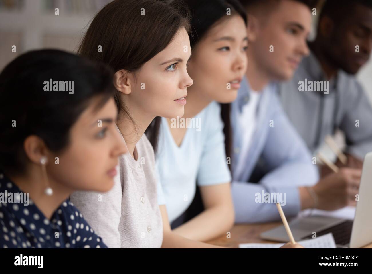 Focused group of mixed race students sitting together at lecture. Stock Photo