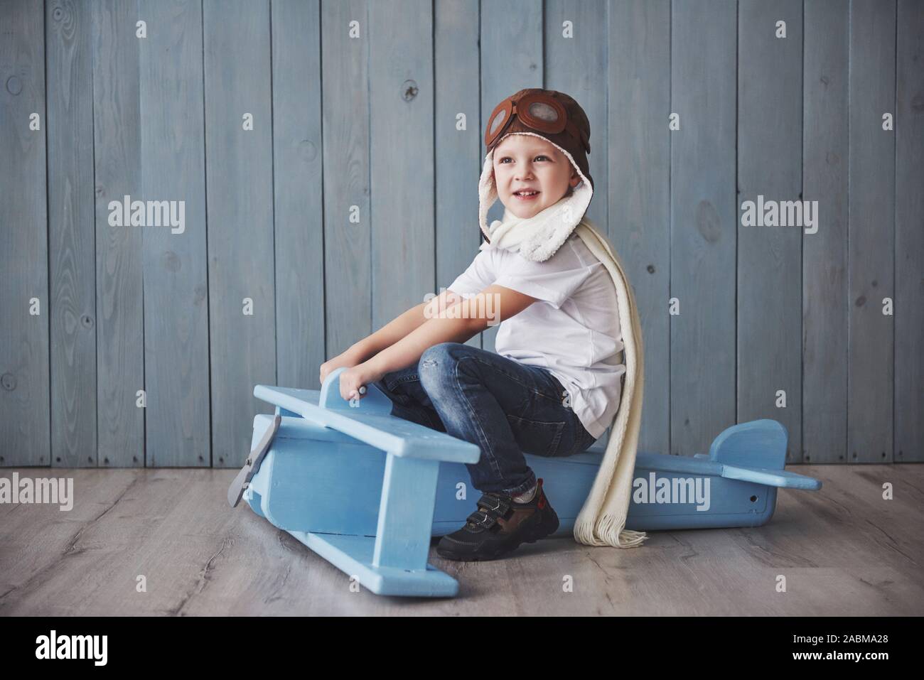 Happy kid in pilot hat playing with wooden airplane against. Childhood ...