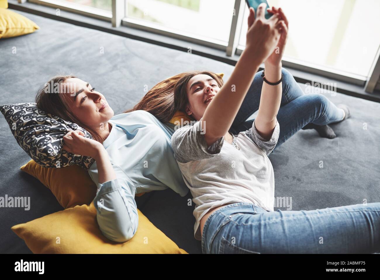 Two cute smiling twins sisters holding smartphone and making selfie 