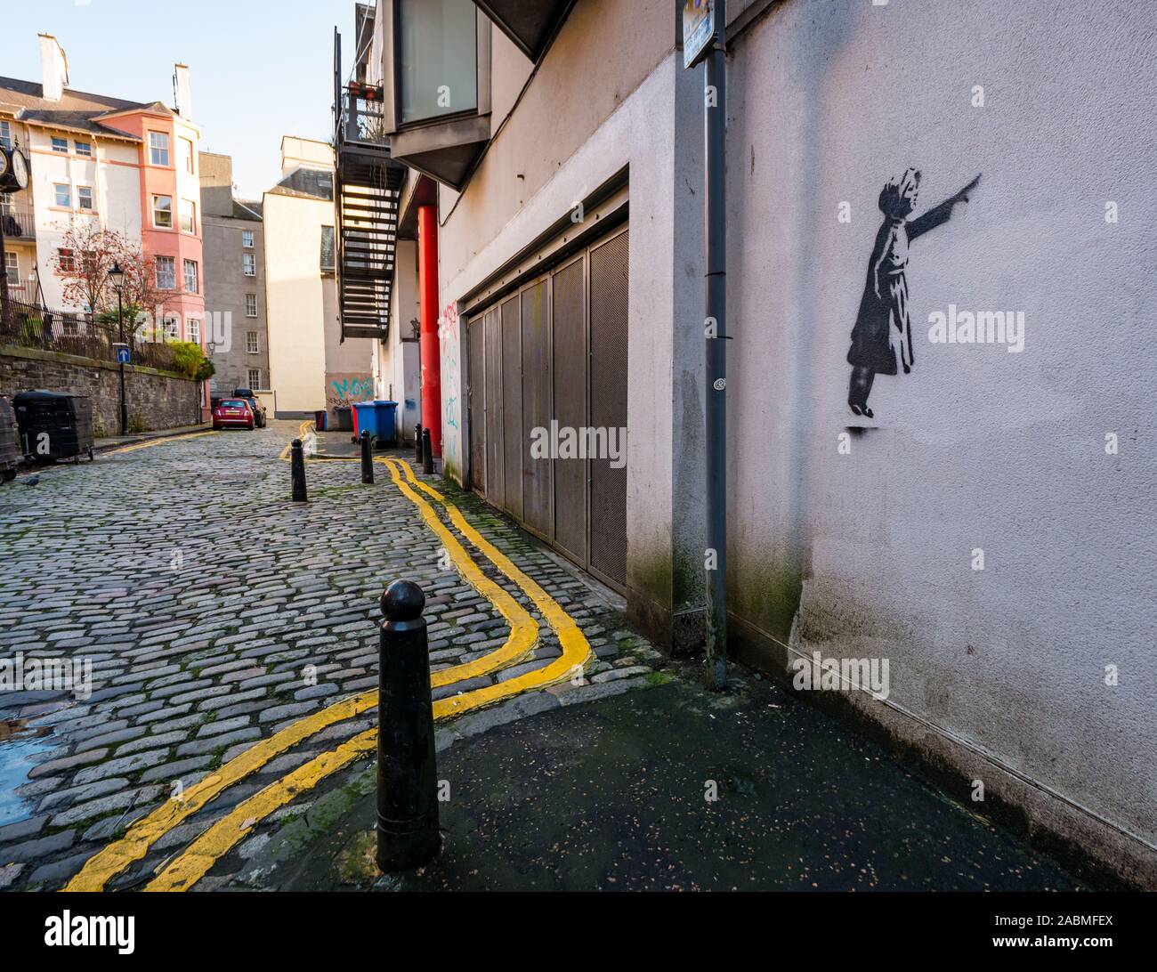 Tron Square, Edinburgh, Scotland, United Kingdom, 28th November 2019. Real of fake Banksy? A stencil of a young girl pointing is discovered on a wall in a quiet narrow cobbled lane. A number of Banksy style stencil images have appeared around the city over the last year but it is unclear whether they are real or copycats Stock Photo