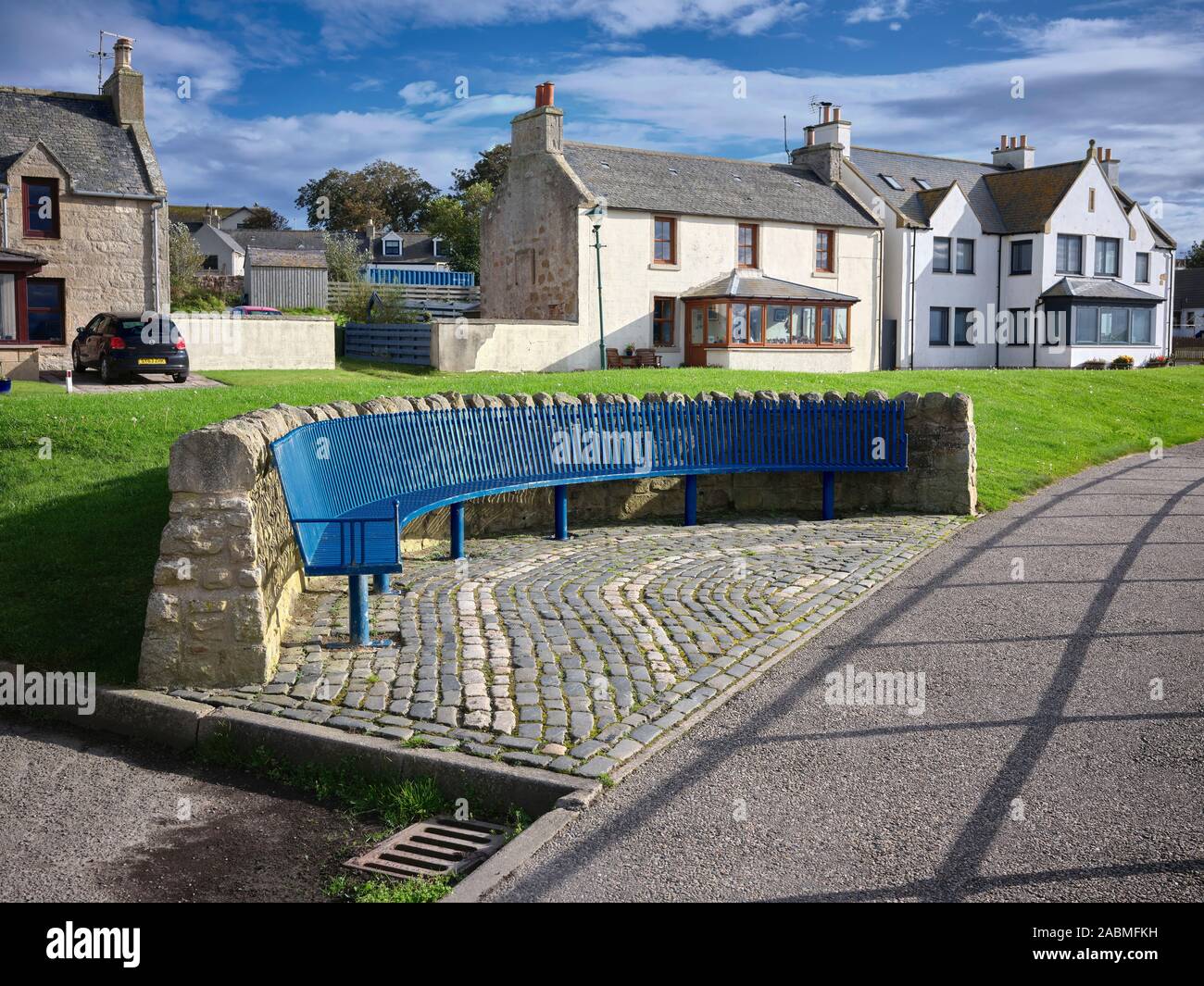 A decorative, blue painted iron sea front seat backed by stone wall and traditional cottages Portmahomack. 26/09/19 Stock Photo