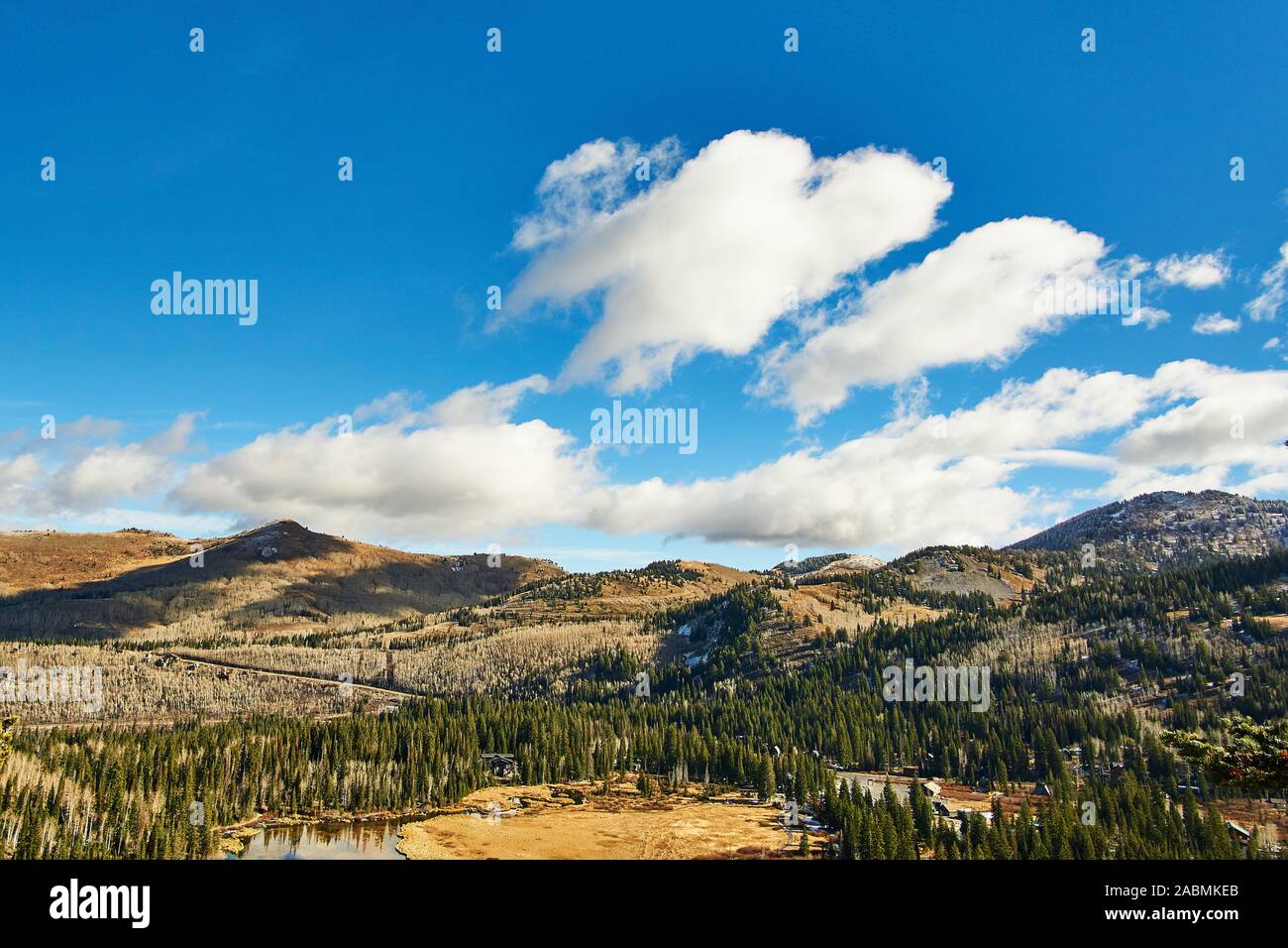 Autumn day at Silver Lake in Brighton, Utah, USA. Clouds in a bright blue sky cast shadows on the forested mountains. Stock Photo