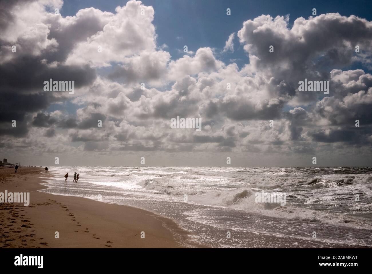 Menschen am Strand bei stuermischer See unter Wolken im Gegenlicht Stock Photo