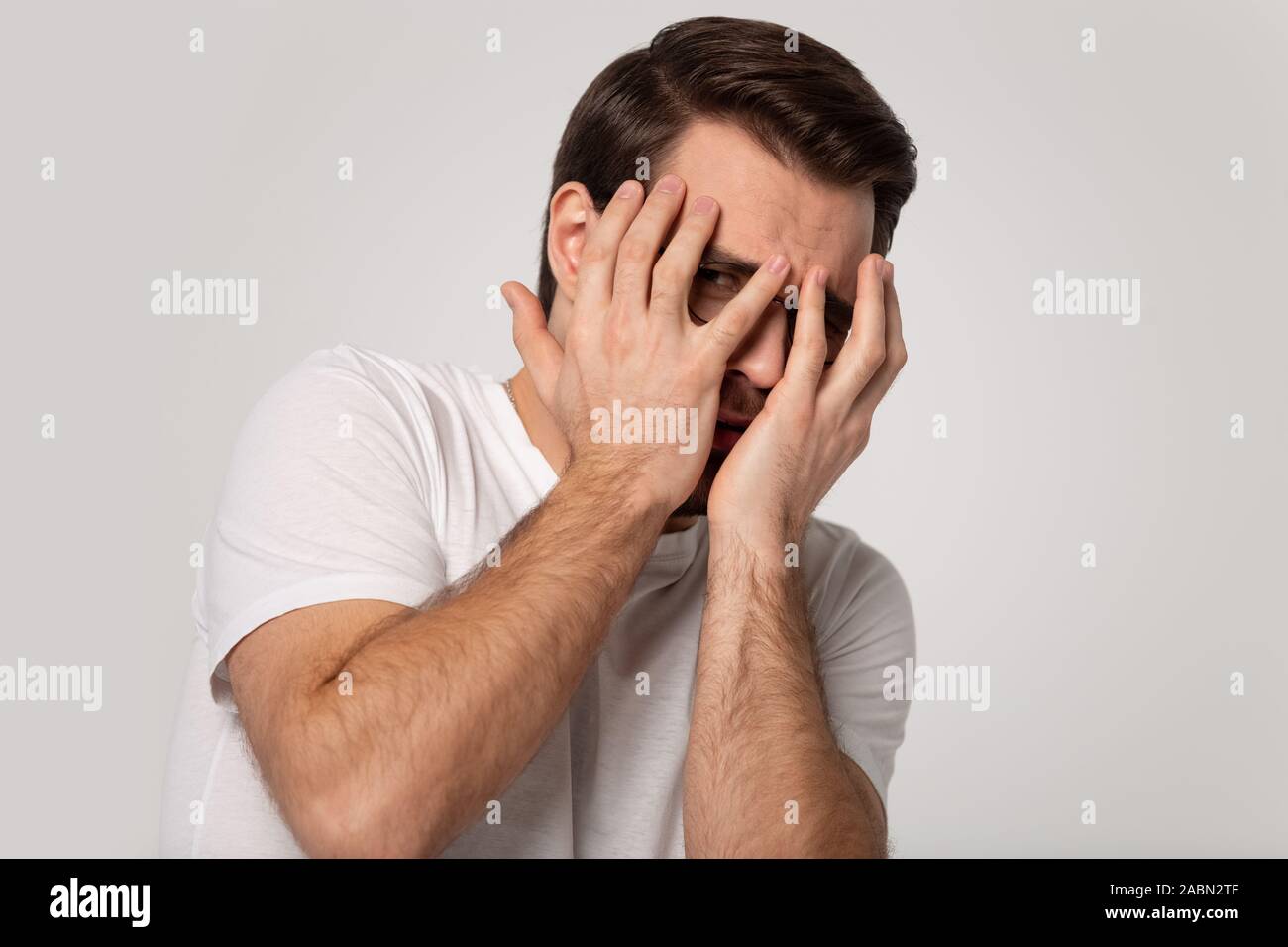 Scared Caucasian man cover face peeping through fingers Stock Photo