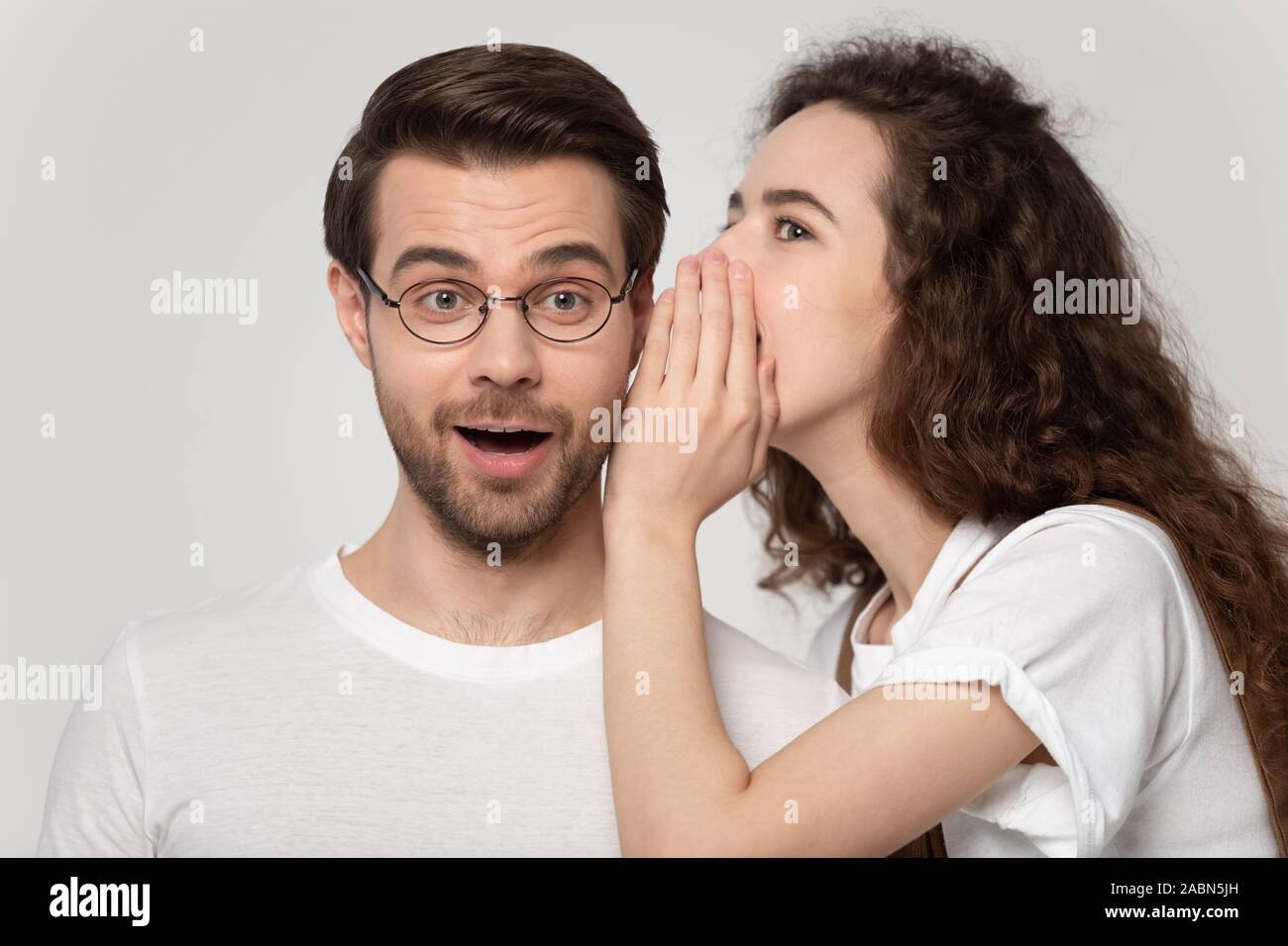 Millennial girl whisper secret in amazed boyfriend ear Stock Photo