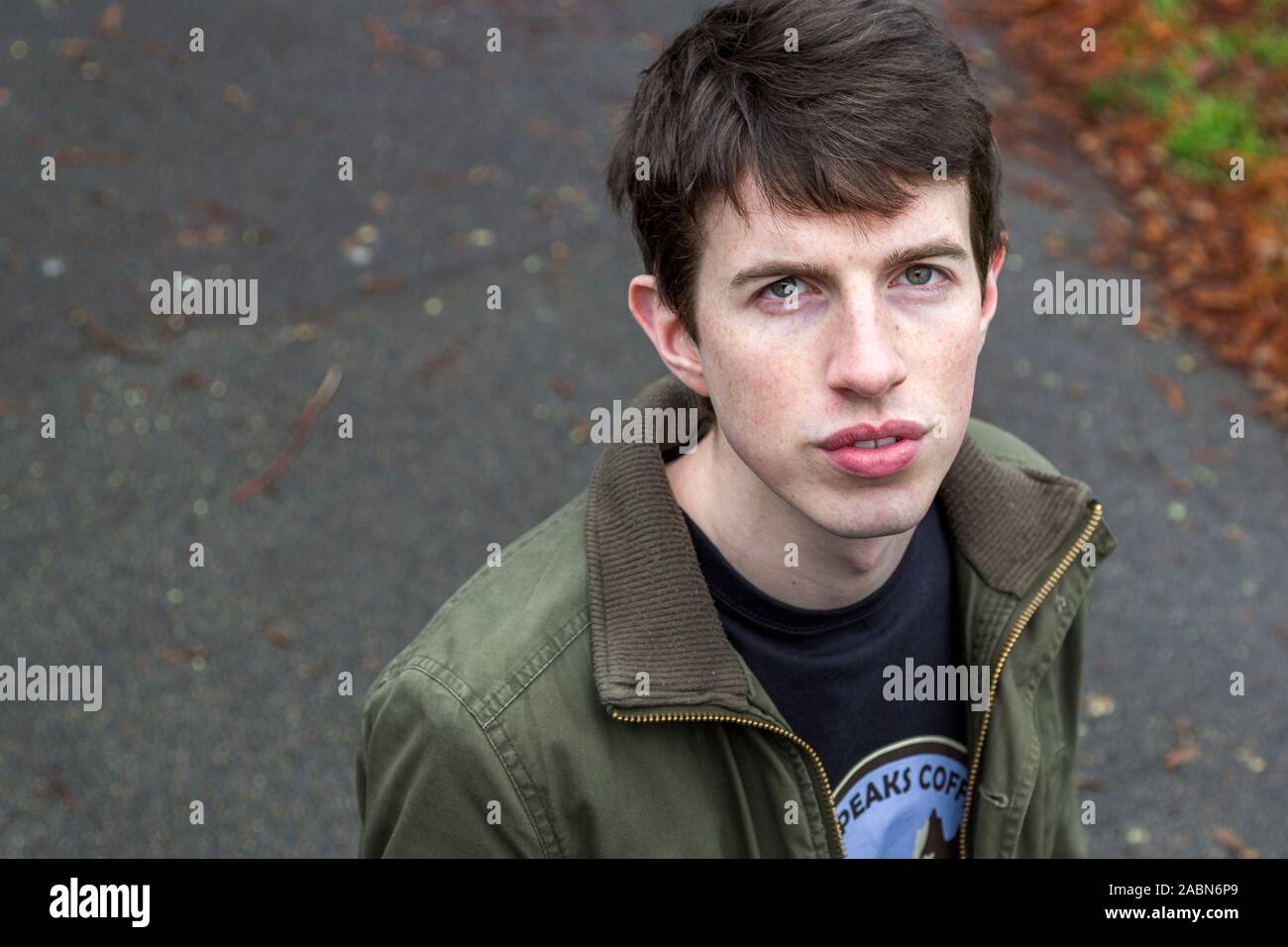 An attractive young man in his late teens or early twenties stands in a park looking up at the camera. Stock Photo